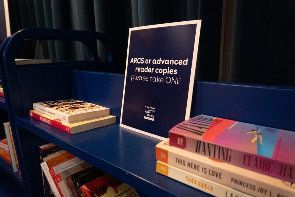 A book shelf with books and a sign reading "ARCS or advanced reader copies please take one".